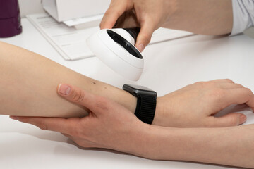 Fototapeta premium Close-up of a dermatologist examining a mole on a female patient's arm using a magnifying glass at a table in a clinic