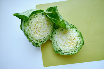 Obraz premium Sliced green cabbage on a light background. Ripe organic farm vegetables. Seasonal vegetables from the garden. Healthy food, vitamins. Organic products selected by hand