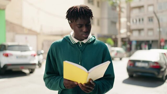 African american man standing with relaxed expression reading book at street