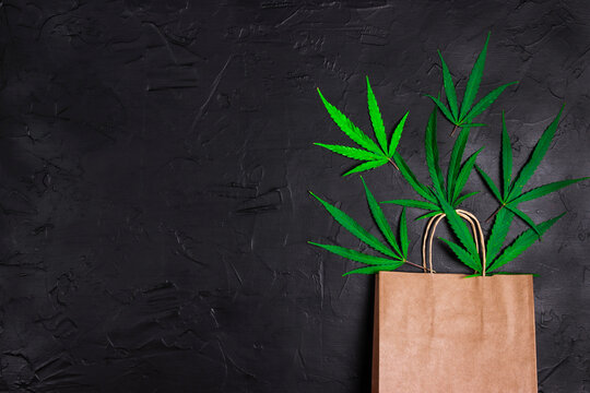 Brown paper shopping bag with green marijuana leaves on black background. Copy space for text.