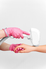 Laser hair removal on the hand on a white background. Pink gloves hold the epilation device on a...