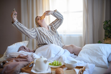 Happy overweight woman with book having breakfast in bed at home.