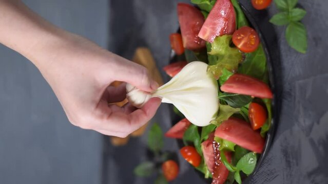Serving burrata cheese on the salad with lettuce, spinach and tomatoes with spices and olive oil. Vertical video
