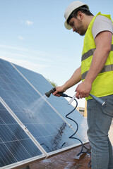 Technician washing solar panels with a hose.