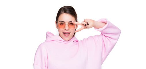 Happy girl in hoodie and pink glasses showing v-sign two fingers gesture isolated on white, peace