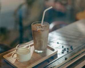 A tall glass of iced latte coffee with milk cream on a wooden counter bar over a cafe glass window reflex at a Cafe coffee shop. Cold brew refreshment summer drink with copy space Selective focus