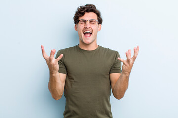 young handsome man furiously screaming, feeling stressed and annoyed with hands up in the air...