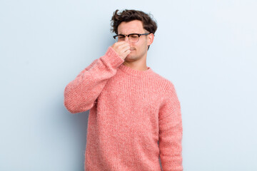 young handsome man feeling disgusted, holding nose to avoid smelling a foul and unpleasant stench
