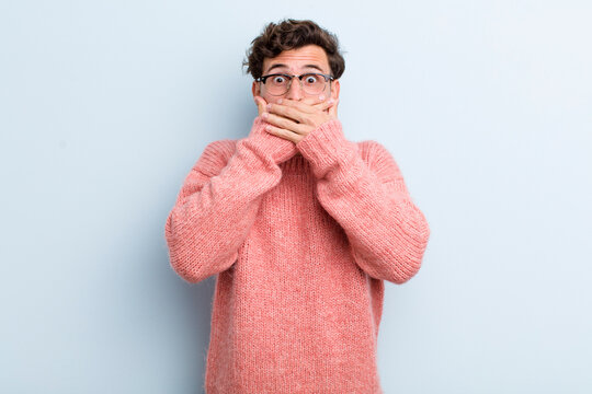 young handsome man covering mouth with hands with a shocked, surprised expression, keeping a secret or saying oops