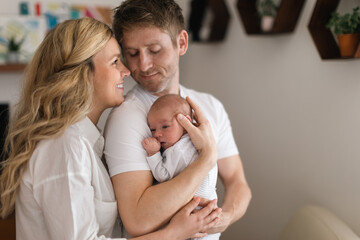Smiling mother and father holding their newborn baby daughter at home