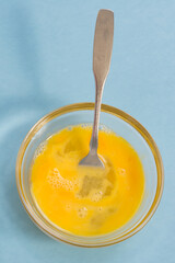 Close up of a raw yellow chicken egg whisked up with froth in a small glass bowl