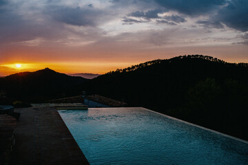 A large rectangular infinity pool with sunset and black mountains in the background. - Powered by Adobe