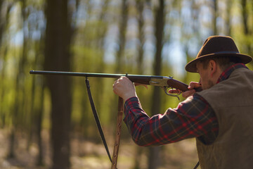 Hunter man aiming with rifle gun on prey in forest.