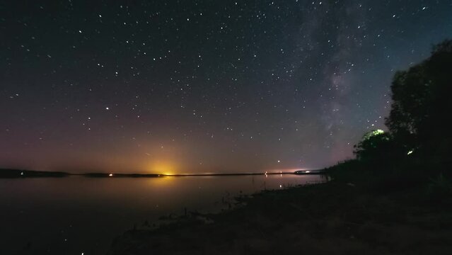 Starry sky timelapse with flat calm lake at night. Milky way is visible in night sky. Space, galaxy, earth moving