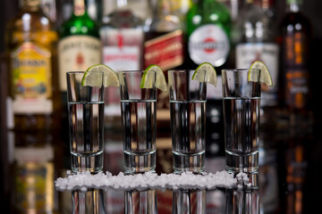 Close-up of a shots of tequila with lime and salt in a bar against the background of shelves with bottles of alcohol.