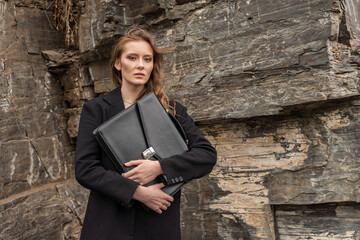 Confident businesswoman stands with a black briefcase. A strong female entrepreneur looks ahead...