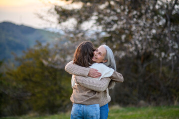 Happy senior grandmother with teenage granddaguhter hugging in nature on spring day.