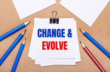 On a light brown background, blue and red pencils and white paper with the text CHANGE AND EVOLVE