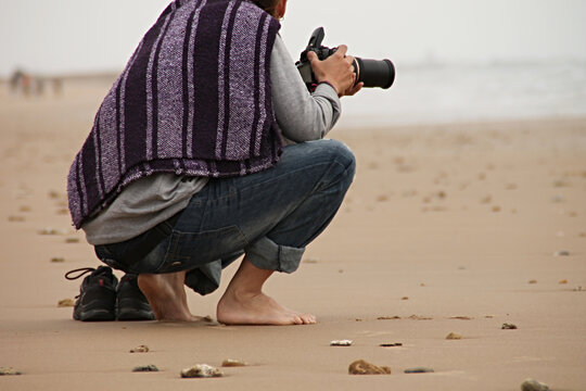 Persona agachada haciendo fotos en la playa con una c&aacute;mara reflex