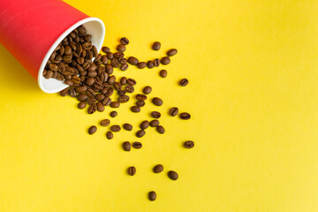 Takeaway red paper coffee cup on yellow background with pouring roasted beans out of it
