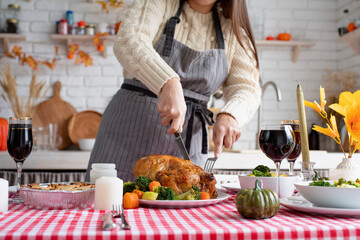 Woman in sweater and apron cutting turkey for family dinner at home kitchen