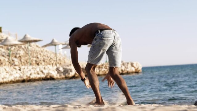 Handsome black young man topless dancing break dance, jumping, handstand, spinning, posing upside down on sand beach 
