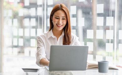 Portrait of happy Asian businesswoman using laptop computer while working with using a calculator to calculate the numbers, finance accounting concept