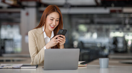 Photo of the adorable young lady working on laptop computer and holding smartphone at office indoors, Asian business woman.