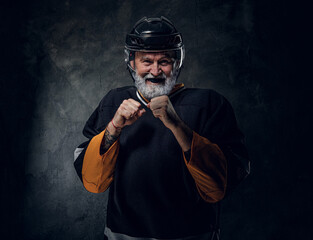 Portrait of ready to challenge aged sportsman dressed in hockey sportswear against dark background.