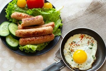 Fried eggs in a frying pan and fried sausages with vegetables and salad