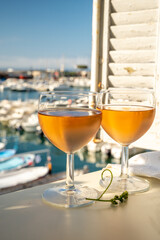 Cold rose wine in glasses served on outdoor terrace in sunlights with view on old fisherman's harbour with colourful boats in Cassis, Provence, France