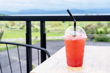 Refreshing drinks for summer, ice berry juice in a plastic cup with blurred green background....