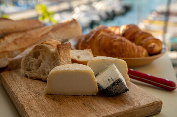 Sunny morning in Provence, breakfast with fresh baked croissants, baquett bread, crottin goat cheese and view on fisherman's boats in harbour of Cassis, Provence, France