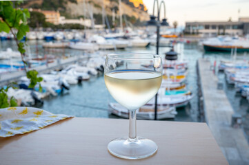 Cold white wine from Cassis region served in glass on outdoor terrace with view on old fisherman's harbour with colourful boats in Cassis, Provence, France