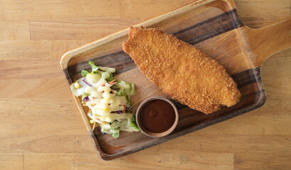 Dolly fish steak served on wooden platter with traditional dressing and vegetable. Breaded dolly fish served with spicy dipping sauce or gravy. top view of dishes
