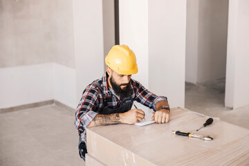 A repairman writing down calculations for material at new apartment in construction process.