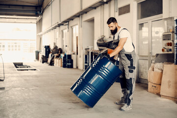 A factory worker rolling barrel with oil and relocating it in facility.