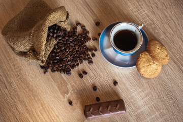 Roasted coffee beans in little bag and cup of coffee with drink on dark wooden surface, nearby lies...