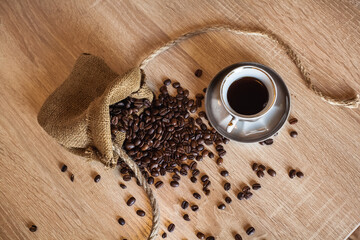 Roasted coffee beans in little bag with ropes and cup of coffee with drink on dark brown wooden...