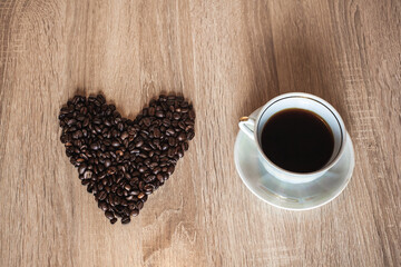 A cup of hot aromatic coffee in a saucer, against the background of scattered coffee beans in the...