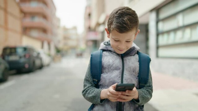 Blond child student using smartphone walking at street