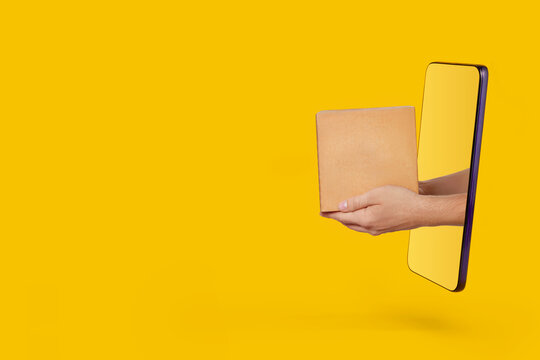 Male hands holding out parcel from modern smartphone on yellow background. Online shopping, service and delivery concept.