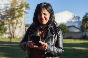 Latin mature woman on the farm, outdoors smiling and texting on her phone.