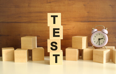 Four wooden cubes stacked vertically on a brown background form the word TEST.