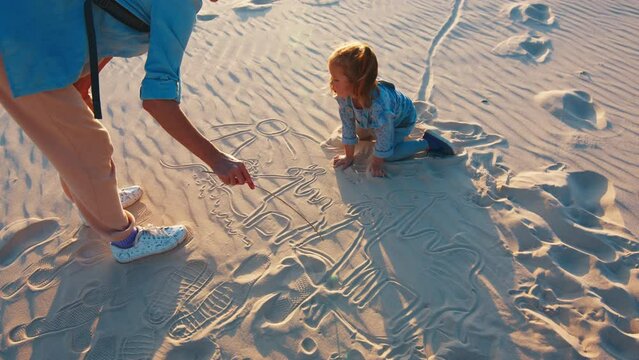 Woman draws pictures on the sand with her kid crawling around