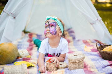 Beautiful girl with a body art face painting butterfly. A rustic autumn still life with pumpkins in basket. Harvest or Thanksgiving. autumn decor, party.