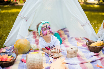 Beautiful girl with a body art face painting butterfly. A rustic autumn still life with pumpkins in basket. Harvest or Thanksgiving. autumn decor, party.