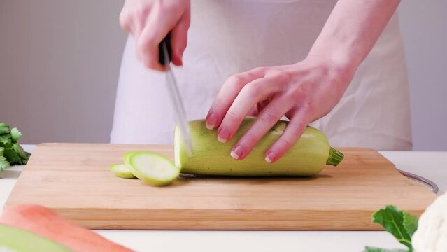 Woman slices courgette into circles on a wooden cutting board on white table