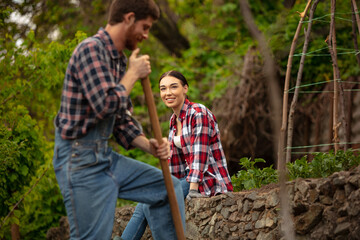 Young and happy farmer's couple at their garden in sunny day. Man and woman engaged in the cultivation of eco friendly products. Concept of farming, agriculture