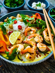 Tom Kha - Thai soup with prawns and rice noodles on wooden table
